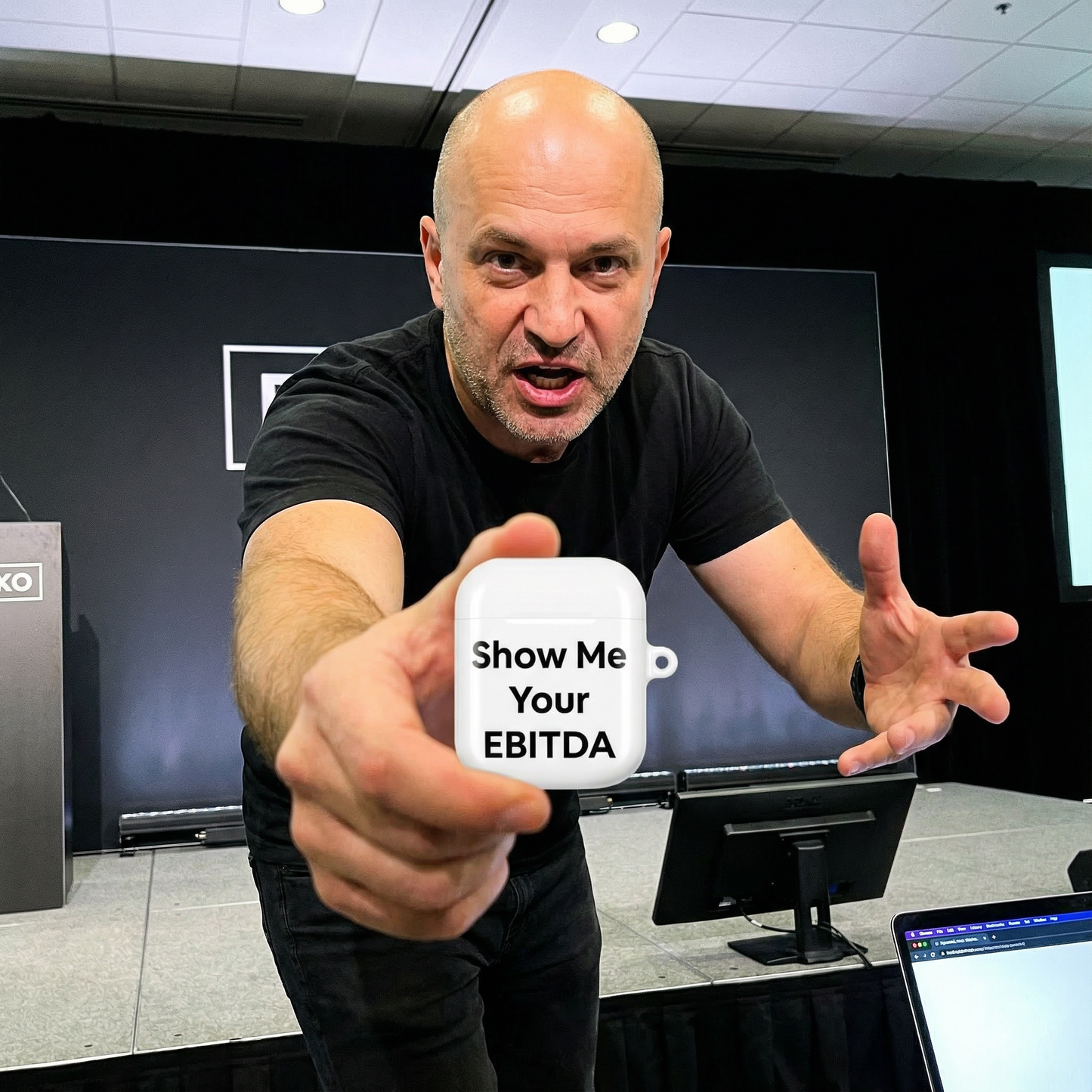 Jargon Junkie white AirPods case with Show Me Your EBITDA text held in office setting corporate humor design